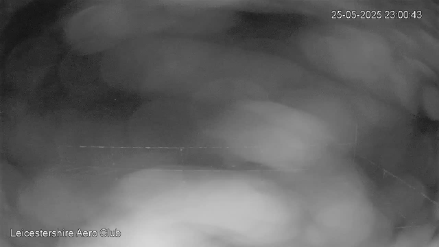 A black and white webcam image showing the inside of an aircraft hangar or maintenance area at night. The image is blurry and mostly dark, with a faint horizontal line running across the middle. The date and time stamp in the upper right corner reads "25-05-2025 23:00:43." The bottom left corner has the text "Leicestershire Aero Club."
