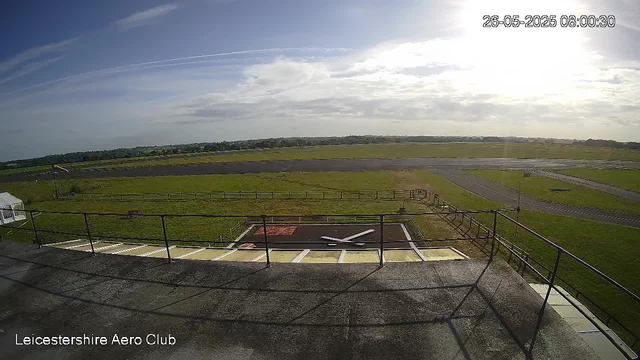 A view from a webcam at Leicesterhire Aero Club showing the runway and grassy fields under a partly cloudy sky with the sun shining, taken in the morning. The timestamp indicates the date as May 26, 2025, at 8:00 AM.