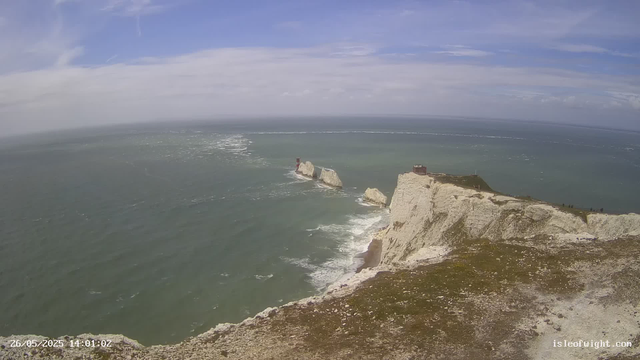 A view of white chalk cliffs overlooking the ocean, with a lighthouse on one of the cliffs and a small building nearby. The sea is calm with some white waves, and the sky is mostly clear with a few clouds. The photo is taken from a high vantage point, showcasing the expansive coastline and open water. The timestamp on the image indicates it was captured on May 26, 2025, at 14:01.