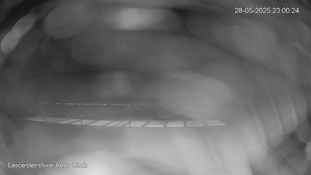 A black and white image from a webcam shows a large, empty indoor space with a high, curved ceiling. The area appears spacious with minimal visible objects, and there is a grid or framework on the floor near the bottom of the image. The corner of the room and some structural elements can be seen along the edges. The timestamp on the top right indicates the date as 28th May 2025 and the time as 23:00:24. The words "Leicestershire Aero Club" are written at the bottom left of the image.