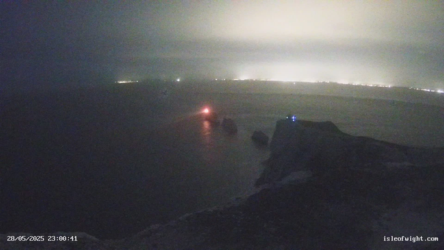 A view from a webcam shows a dark sky over a body of water at night. There are distant lights along the horizon, and a faint glow on the water's surface. In the foreground, part of an airplane wing and some aircraft equipment are visible. The timestamp on the image indicates it was taken on May 28, 2025, at 11:00 PM.