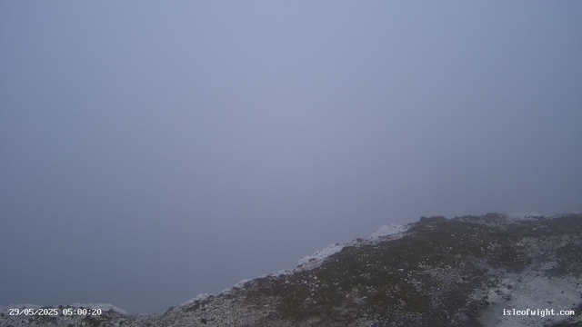 A foggy or misty landscape showing a barren, rocky terrain with patches of snow or ice. The sky is overcast, creating a gloomy atmosphere. There is a timestamp in the bottom left corner and a website URL in the bottom right corner.