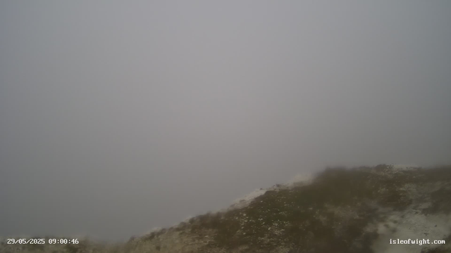 A foggy, overcast scene with limited visibility; part of a rocky or muddy terrain in the foreground; no clear objects or landmarks visible due to thick fog. The timestamp shows "29/05/2025 09:00:46" and the website "isleofwight.com" is displayed in the bottom right corner.