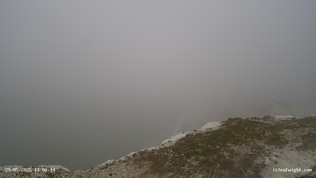 A foggy view over a rocky, uneven surface at the edge of a site, with thick fog obscuring the background and reducing visibility. The image includes a timestamp in the bottom left corner and a website name in the bottom right corner.