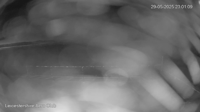 A black and white image taken from a webcam showing a close-up view of two hands with fingers interlaced. The background is blurry, and there is a timestamp in the top right corner reading "29-05-2025 23:01:09." The bottom left corner has text that reads "Leicestershire Aero Club."
