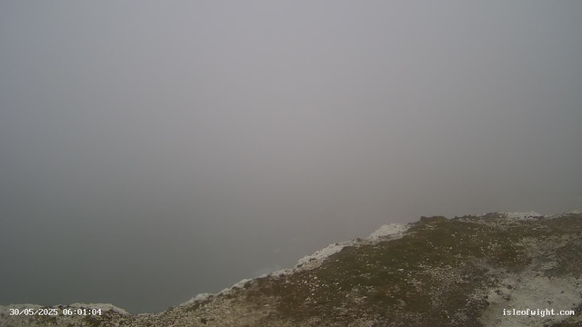 A foggy landscape with a distant horizon obscured by dense fog, and a rocky or grassy foreground with patches of white, possibly snow or salt. The sky is overcast, blending into the fog. The timestamp in the lower left corner indicates the date and time as May 30, 2025, at 6:01 AM.