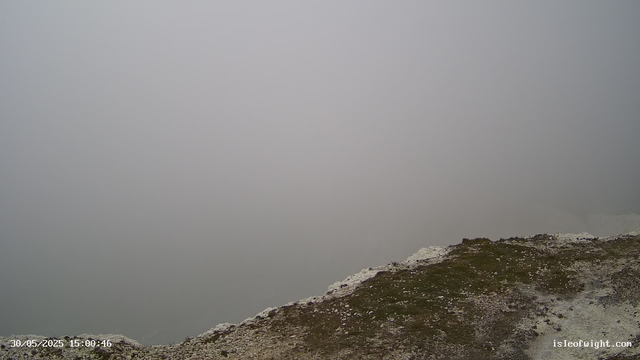 A foggy or cloudy landscape at the top of a mountain or hill, with a rocky, uneven terrain at the edge. The sky and background are obscured by dense fog or low clouds, giving an impression of high elevation and misty weather. The timestamp in the bottom left corner reads "30/05/2025 15:00:46" and the website "isleofwight.com" is visible in the bottom right corner.
