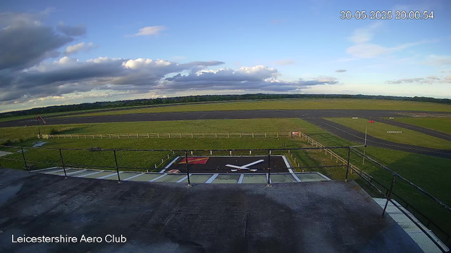 A view from a webcam showing the sky with scattered clouds and a landscape of grassy fields and distant trees. In the foreground, there is a helipad marked with a large red letter "H" enclosed by a black border, and the "Leicestershire Aero Club" is labeled at the bottom of the image. The image is timestamped "30-05-2025 20:00:54."