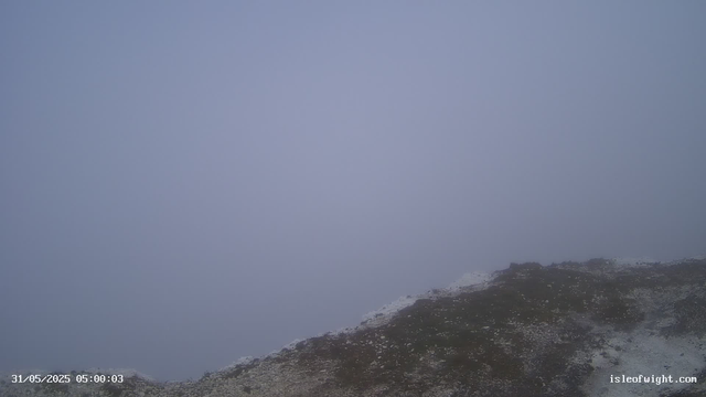 A foggy landscape with a rocky, uneven terrain in the foreground. The sky is overcast and visibility is limited due to thick fog. The horizon and any distant features are obscured by the dense mist. The bottom left corner shows a timestamp and date, and the bottom right corner displays a website URL.