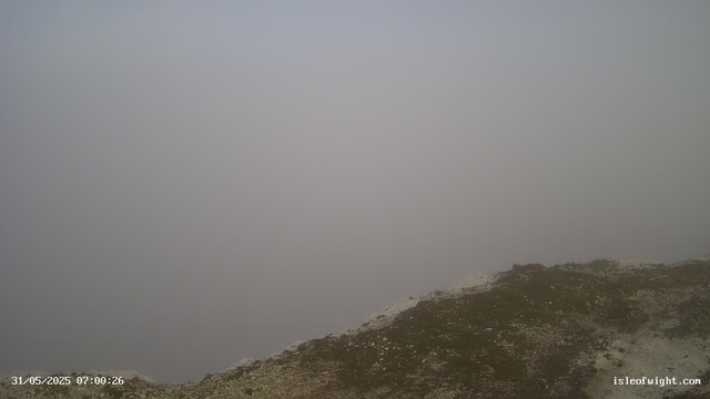 A foggy landscape with a rocky, uneven surface in the foreground. The sky is overcast and visibility is low due to dense fog, obscuring the background. The timestamp on the image reads "31/05/2025 07:00:26" and the website "isleofwight.com" is displayed in the bottom right corner.