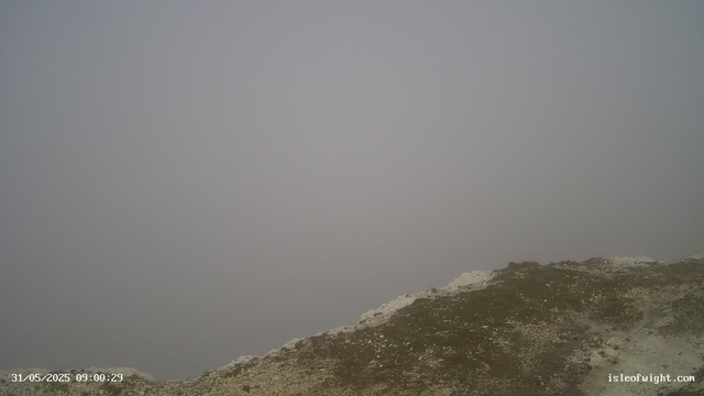 A foggy landscape with a rough, rocky terrain at the bottom of the image. The sky is completely overcast with dense fog, obscuring any distant views. The image includes a timestamp in the lower left corner and a website URL in the lower right corner.
