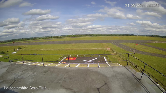 A view from a webcam at Leicestershire Aero Club showing a cloudy sky over an empty airfield with runways and grassy areas, taken on May 31, 2025, at 15:00:41. The foreground includes a helipad with painted markings and a railing along the edge of a building or observation deck.