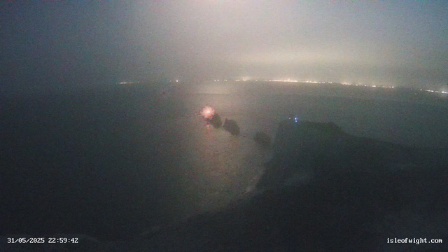 A nighttime view from a webcam shows a dark, likely coastal scene with faint lights along the horizon, possibly indicating a distant shoreline or city lights. In the foreground, there are indistinct structures or objects, with one emitting a small bright light. The image is somewhat blurry and has a grainy texture due to low light conditions. The timestamp at the bottom left reads "31/05/2025 22:59:42," and there is a website link "isleofwight.com" at the bottom right.