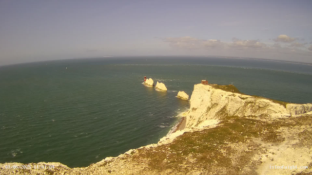 A view of white chalk cliffs extending into the ocean, with two prominent lighthouse structures on separate rocks and atop the cliffs. The water is a deep green, and the sky is partly cloudy with a horizon visible in the background. The timestamp on the image shows "01/08/2023 11:01:04."