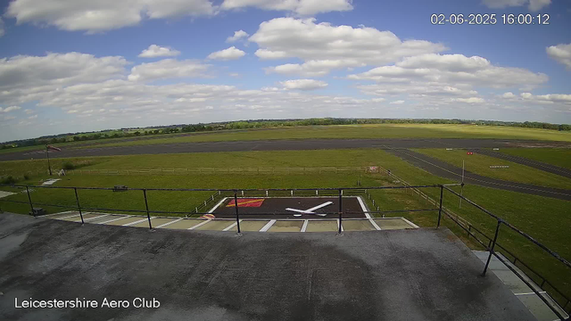 A wide view of an airfield with a small helicopter pad in the foreground, a grassy area, runways, and open sky with fluffy white clouds. An American flag is visible on the left side. The timestamp shows the date as February 6, 2025, at 4:00 pm and 12 seconds. The bottom left corner has the text "Leicestershire Aero Club."