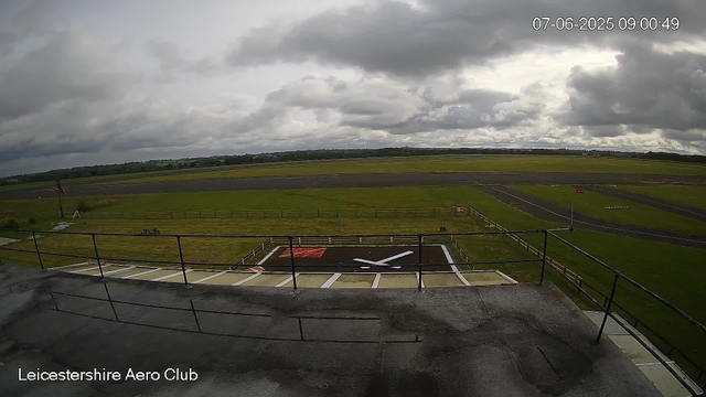 A view of an airfield with a helicopter landing pad in the foreground, surrounded by grassy areas and runways stretching into the distance under a cloudy sky. The timestamp shows the date as July 6, 2025, at 9:00 AM. The bottom left corner indicates the location as Leicesterhire Aero Club.