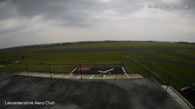 Overcast sky with dark clouds at Leicestershire Aero Club, showing a lawn and runway with cloudy weather. The image has a time stamp of 09-06-2025 13:00:54.