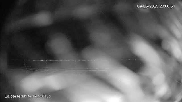 A black-and-white, blurry image from a webcam showing some indistinct shapes and textures. The timestamp in the upper right corner reads "09-06-2025 23:00:51". The bottom left corner contains the text "Leicestershire Aero Club".