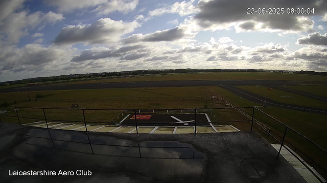 A wide view of an airfield under a partly cloudy sky, with a helicopter landing pad and grassy areas in the foreground. The image is timestamped June 23, 2025, at 8:00 AM, and is labeled "Leicestershire Aero Club."