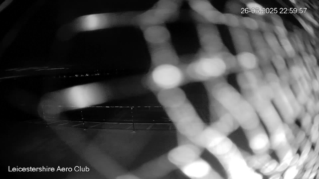 A black and white image showing a close-up of a sports car's front grille, with reflections and details of its design. The top right corner displays a timestamp: "26-06-2025 22:59:57," and the bottom left corner has the text "Leicestershire Aero Club."