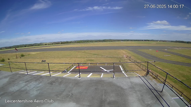 A wide view of an aerial area at Leicestershire Aero Club showing a tarmac runway in the background under a partly cloudy blue sky. In the foreground, there is a small parking area with white and yellow lines, a red and yellow marking, and a wheelchair accessible space. A metal railing borders the platform, with a person standing near the railing on the right side. Fields and open land extend beyond the runway, and a red windsock is visible on the far left side. The timestamp indicates the date as June 27, 2025, at 14:00:17.