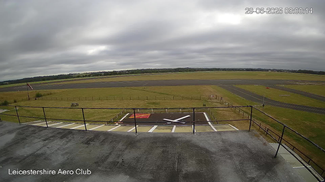 An overcast sky above an empty airfield with a runway stretching into the distance. In the foreground, there is a helipad marked with a large red "H" and a black and white striped pattern, surrounded by a safety railing. The image includes a timestamp in the top right corner (29-06-2025 08:00:14) and a label in the bottom left corner that reads "Leicestershire Aero Club."