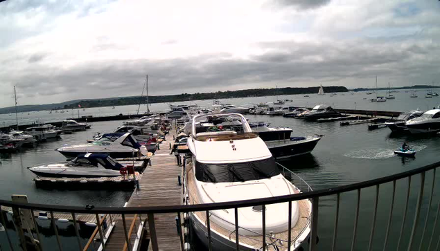 A marina filled with various boats docked along wooden piers, with some boats out on the water, and a cloudy sky overhead.
