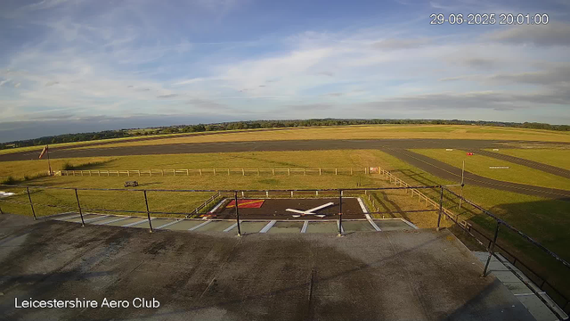 The image shows the Leicesterhire Aero Club's helipad with a large "H" marking in white, situated on a flat concrete surface surrounded by a black metal railing. In the background, there are open fields, runways, and a partly cloudy blue sky. The timestamp in the top right corner indicates it was taken on June 29, 2025, at 8:01 PM. The bottom left corner has the label "Leicestershire Aero Club."