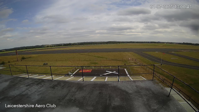 A cloudy sky over an airfield at Leicester Aero Club, with a runway in the distance, some grassy areas, and a helicopter landing pad in the foreground. The date and time stamp read "01-07-2025 13:00:43."