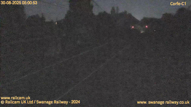 A dark, nighttime scene of a railway track with faint outlines of trees and hills in the background. There are a few small red lights in the distance, possibly signals or lights on buildings, and the overall area appears deserted. The timestamp on the top left indicates the date and time as August 30, 2025, at 05:00:53.