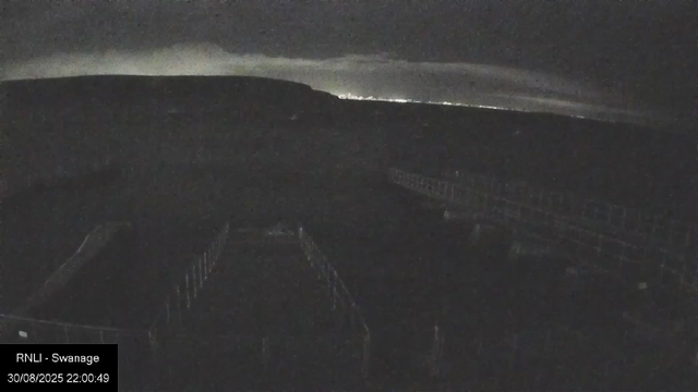 A dark, nighttime view from a webcam showing a bridge or walkway with railings, stretching across a body of water. The sky is cloudy or foggy, and the horizon is barely visible. There is a timestamp and location tag at the bottom left, indicating the image was taken at night on August 30, 2025, in Swansea.