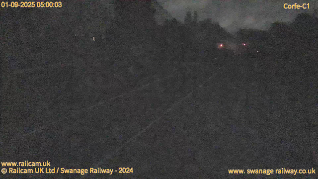 A dark, foggy scene of a railway track at night, with only a few faint red lights visible in the distance. The image appears grainy and low-light, likely captured from a webcam. The timestamp shows "01-09-2025 05:00:03," and there are labels indicating it's from a railway camera in Swansea, UK.