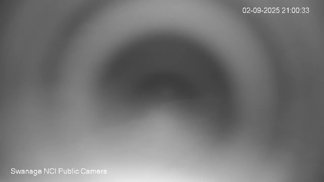 This is a blurry black and white image from a webcam showing a close-up of a circular object or opening. The top right corner displays a timestamp reading "02-09-2025 21:00:33," and the bottom left corner indicates the source as "Swanage NCI Public Camera."