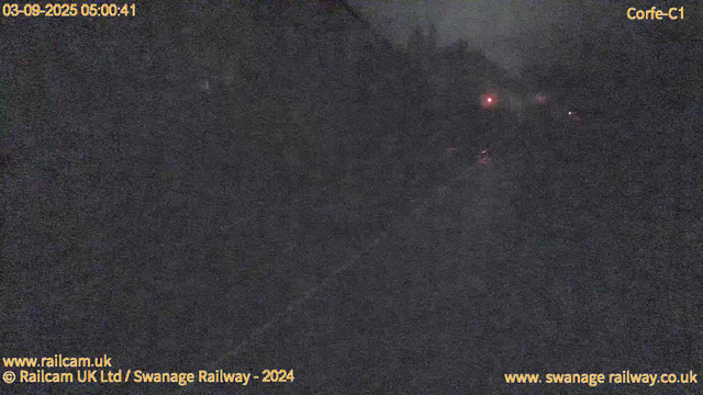 The image is very dark and appears to be taken at night or in low light conditions. It shows a mostly black scene with faint, reddish lights visible in the distance, possibly from distant signals or equipment. There are no clearly identifiable objects or features visible in the image. Text overlays provide the date and time as September 3, 2025, at 05:00:41, and indicate the image is from a webcam on the Swanage Railway, specifically at location Corfe-C1.