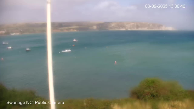 A panoramic view of the sea with several boats scattered across the water. In the background, there are cliffs and a cloudy sky. In the foreground, there is some greenery, possibly trees or bushes. The timestamp in the top right corner reads "03-09-2025 13:00:40".
