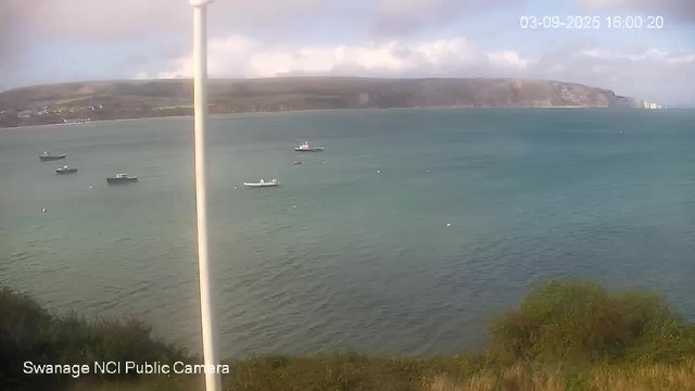 A view of a tranquil bay with several small boats floating on calm water. In the background, there is a hilly shoreline with some buildings visible on the right side. The sky is partly cloudy, and the scene appears to be captured during late afternoon with soft lighting. A vertical white pole partially obscures the left side of the scene. The timestamp on the image indicates the date as September 3, 2025, and the time as 4:00 PM.
