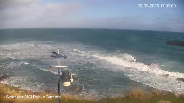 A view of the ocean with waves crashing against the shoreline, under a partly cloudy sky. There is a weather station with an anemometer and other equipment in the foreground on the left side. The date and time displayed in the top right corner are "03-09-2025 17:00:00."