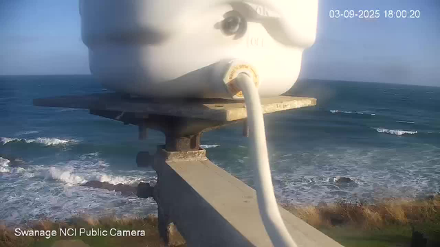 A view from a webcam showing a large white navigation buoy mounted on a metal structure near the coastline, with the ocean and waves in the background. The sky is clear, and the water is a deep blue. The timestamp in the top right corner indicates the date and time as March 9, 2025, at 6:00 PM.